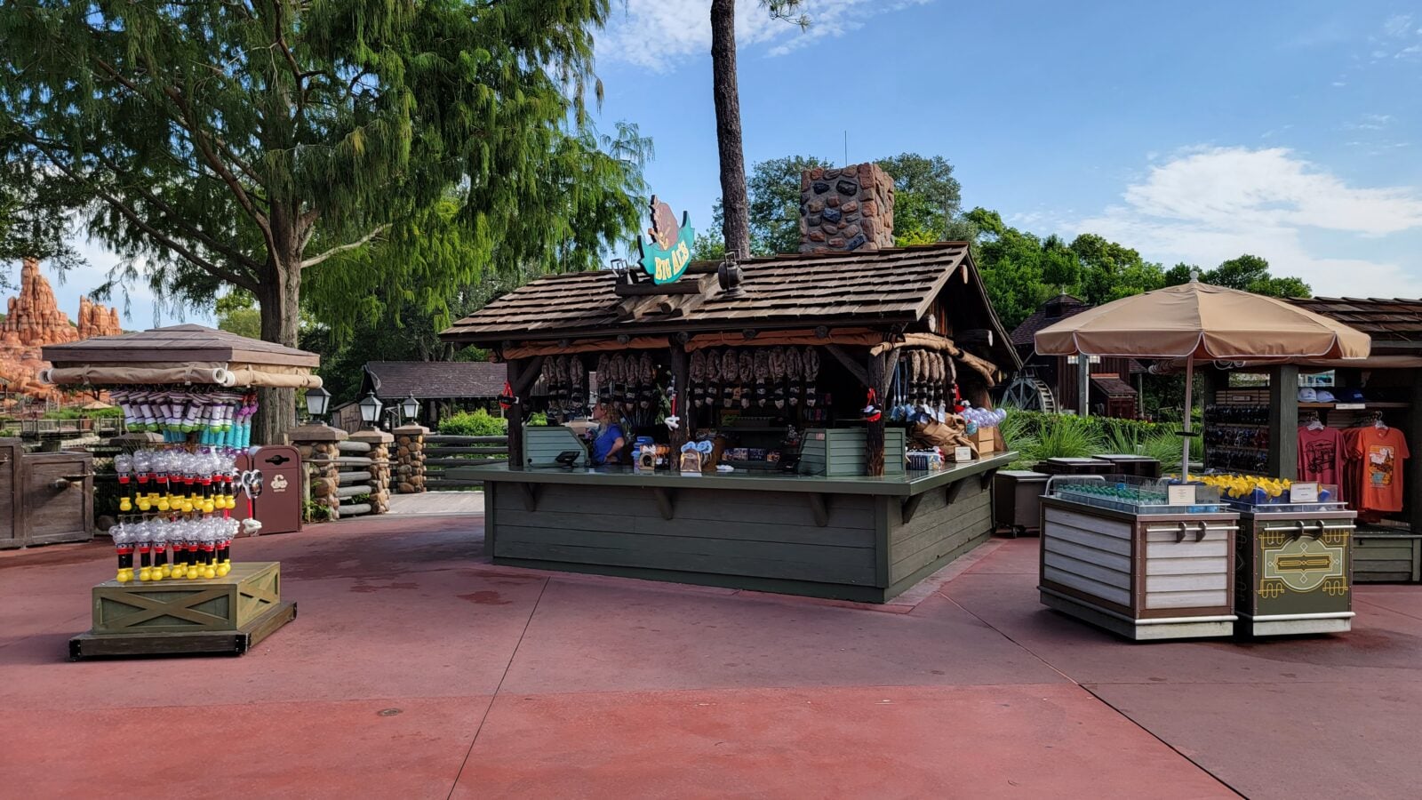 Rustic outdoor market stall with sausages hanging bottled drinks on a rack and a counter under a wooden roof