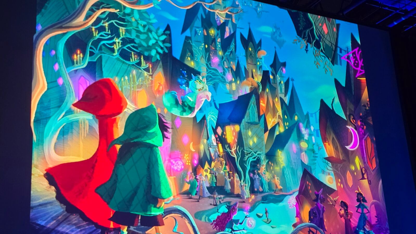 Two hooded figures overlook a vibrant fantasy town with glowing buildings and a festive parade below