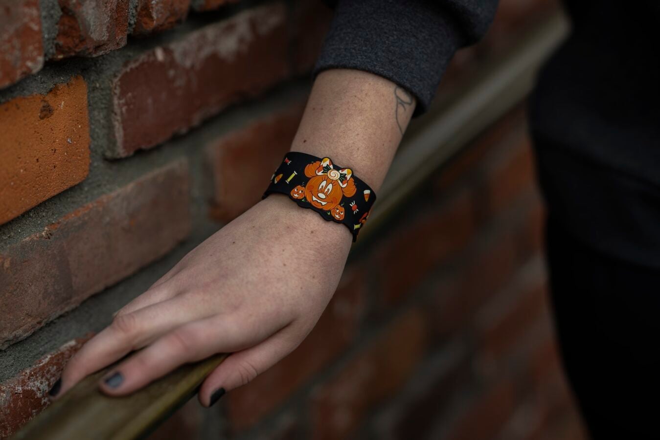 Close up of a forearm wearing a Halloween bracelet with orange pumpkins against a brick wall background