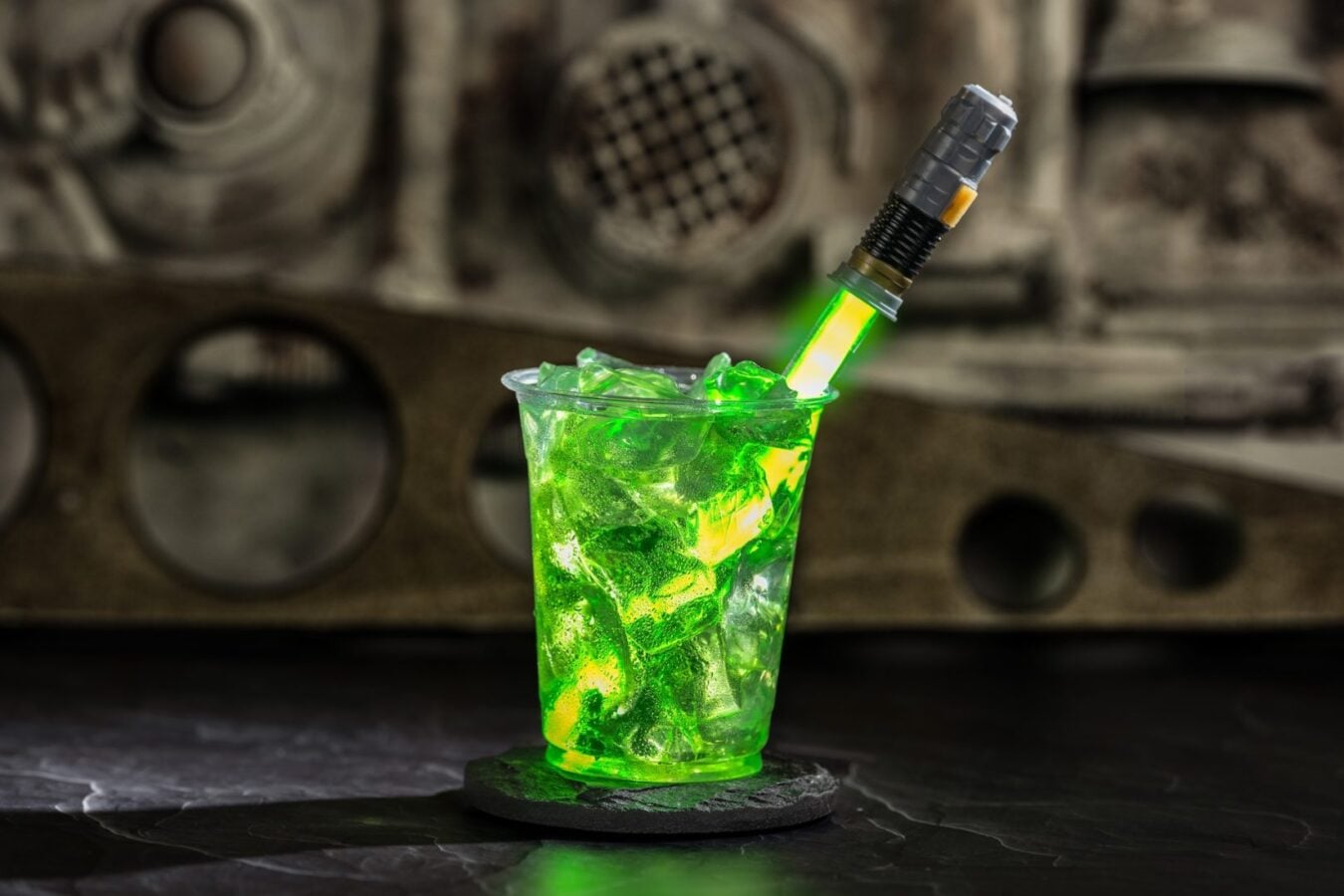 Glowing green cocktail in a clear cup with ice a sci fi looking glowing straw set on a dark bar with an industrial backdrop