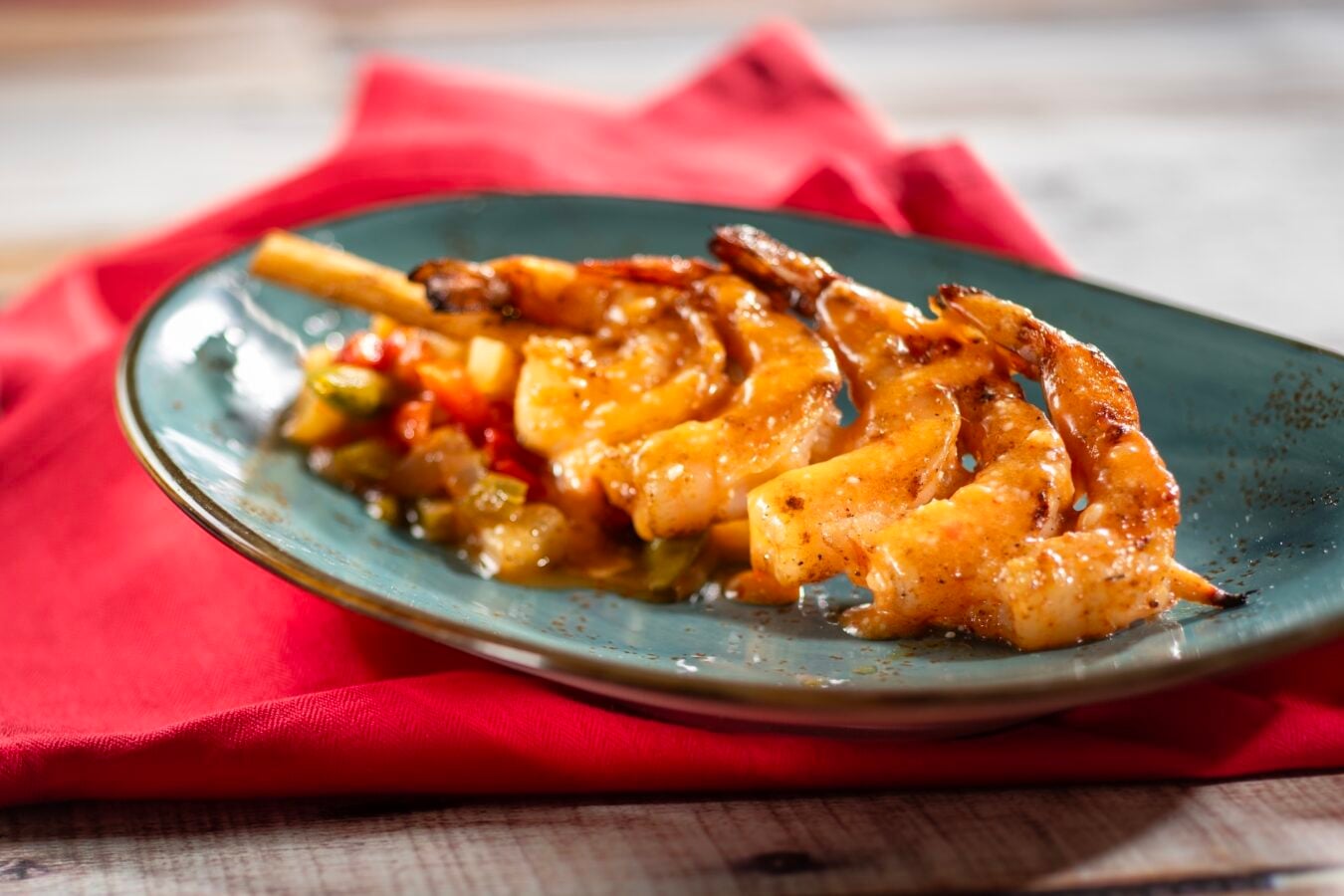 Grilled shrimp with glaze and vegetables on a teal plate resting on a red napkin