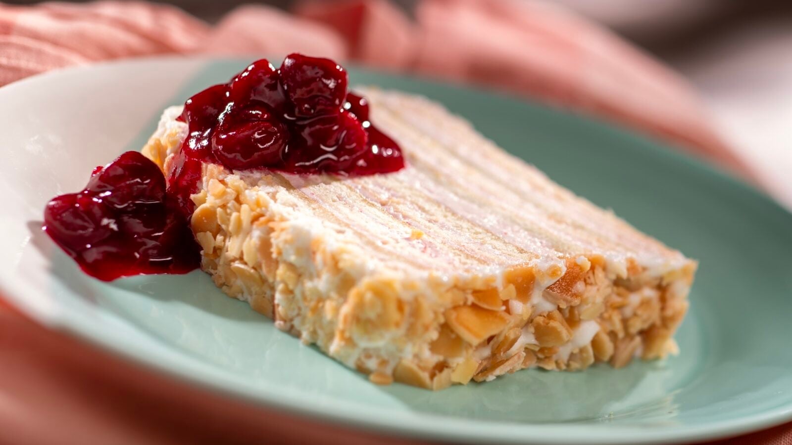 Slice of almond cake with white frosting and cherry sauce on a turquoise plate