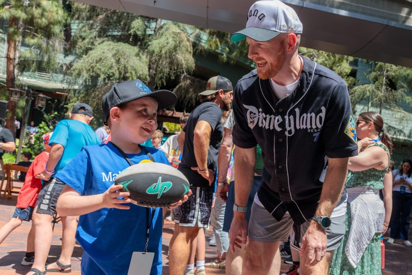 Adult man in a black Minnesota style jersey talking to a smiling young boy holding a football outside at an event
