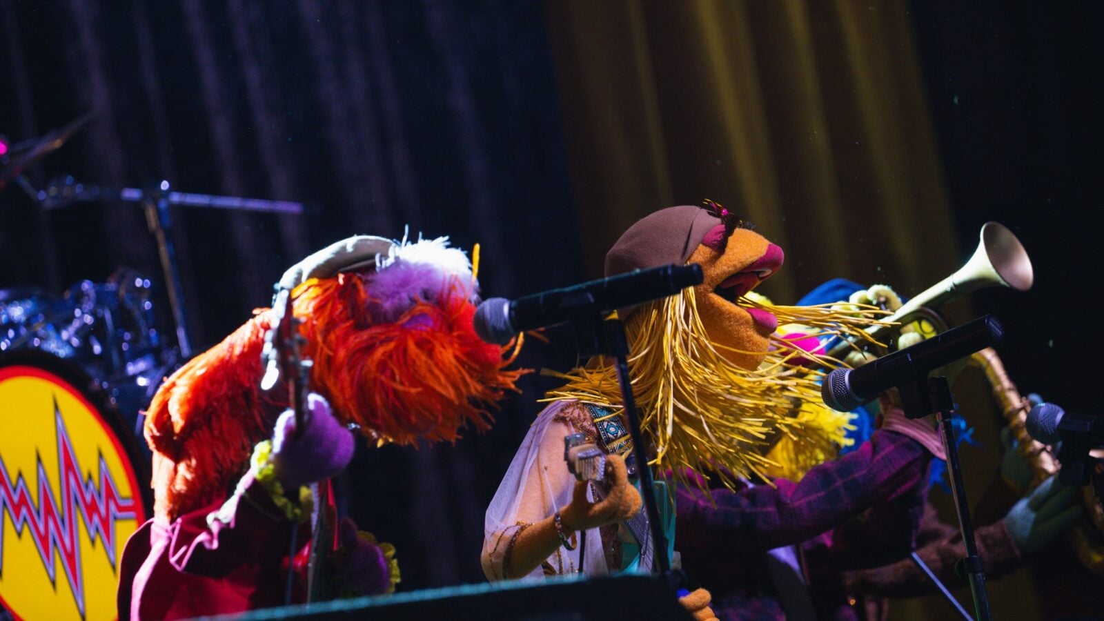 67054075213821448072756711878469132440894984n Fantasy Land News Colorful puppets performing on a stage with microphones wearing bright costumes and long hair like strands