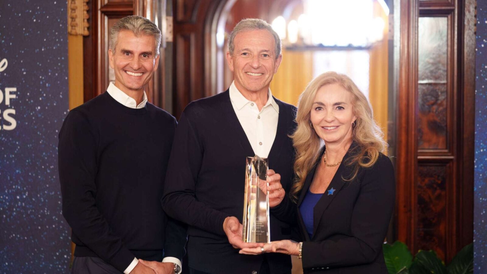 Three adults at an awards ceremony center man holds a tall crystal trophy flanked by a man on the left and a woman on the right