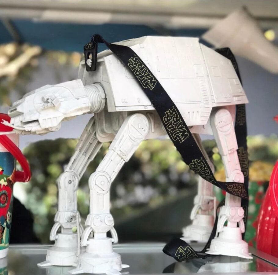 White Star Wars AT AT toy walker with black Star Wars straps draped over its back standing on a glass surface on display