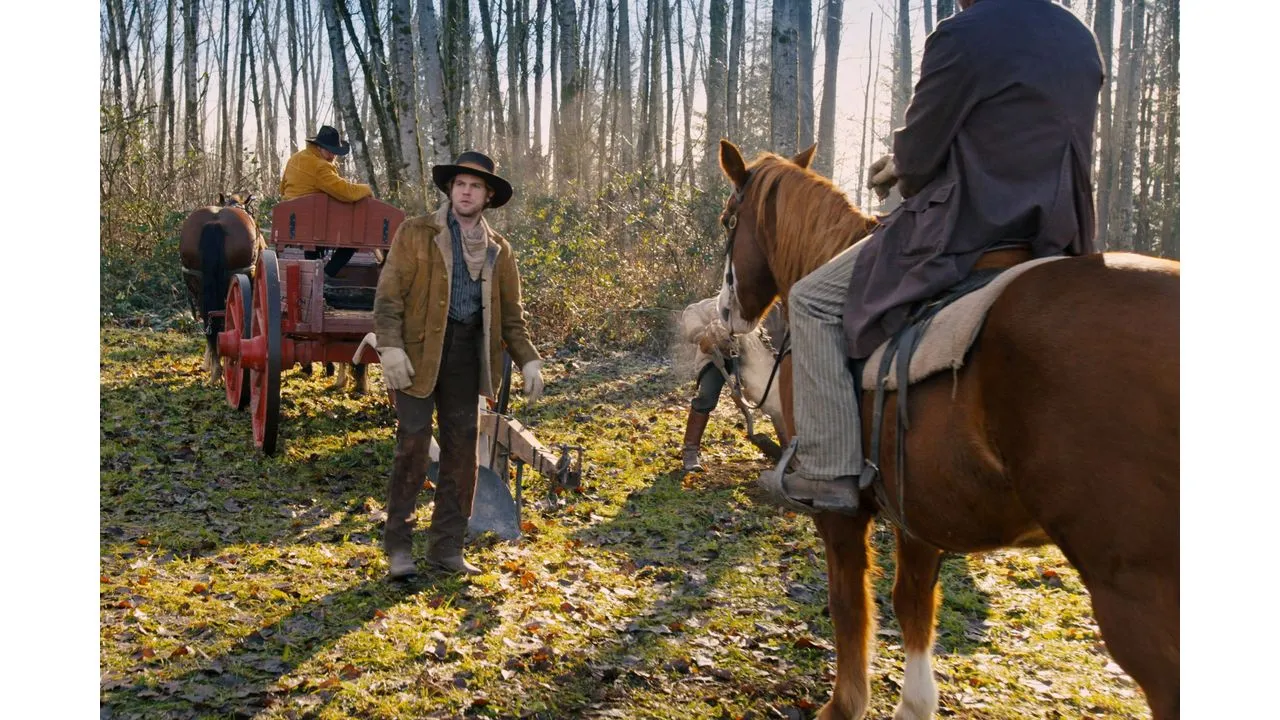 Three men in old fashioned frontier clothing with a red horse drawn wagon in a leaf strewn forest clearing