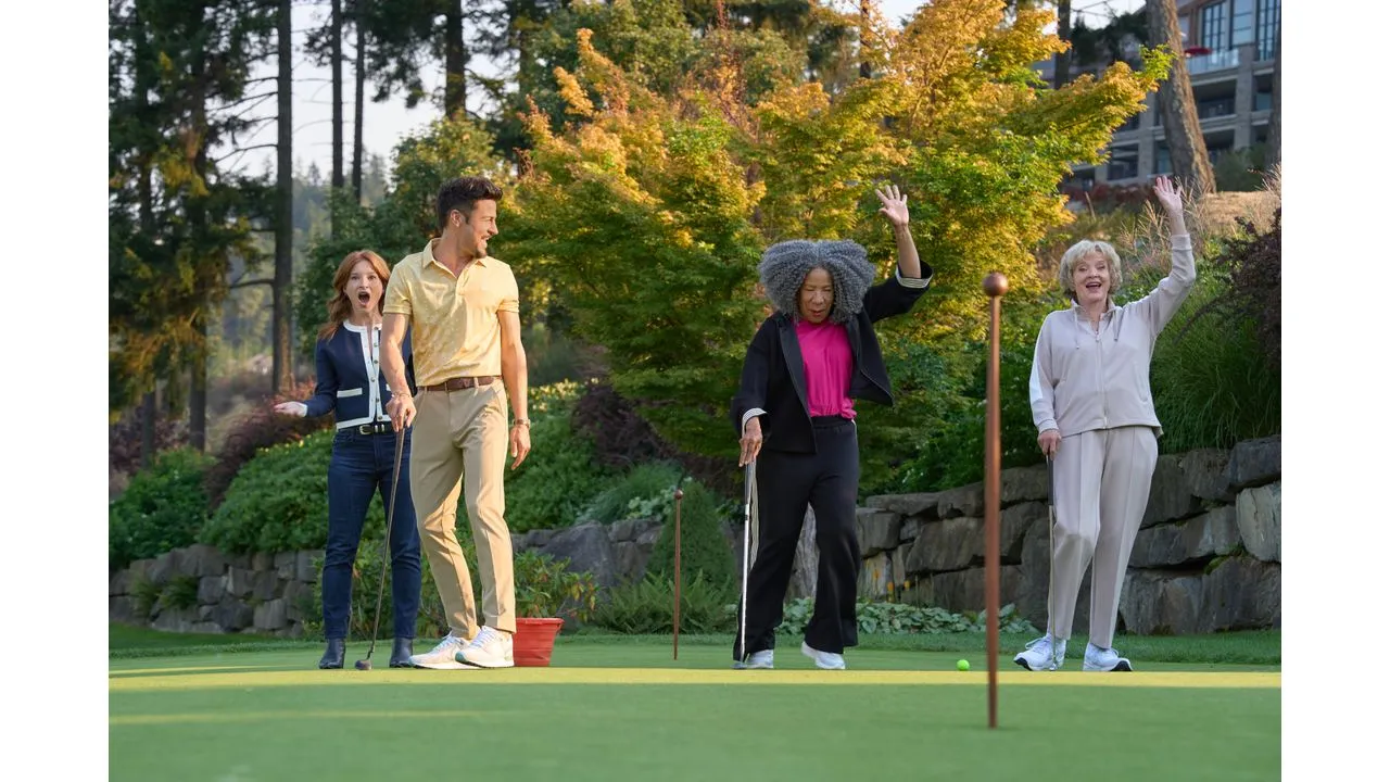 Four adults playing mini golf outdoors on a sunny day with trees and a stone wall in the background