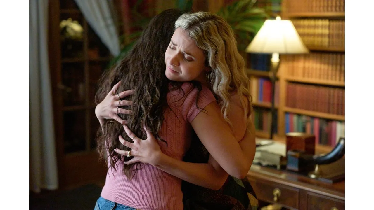 Two women share a comforting hug in a cozy study with a wooden desk and bookshelves