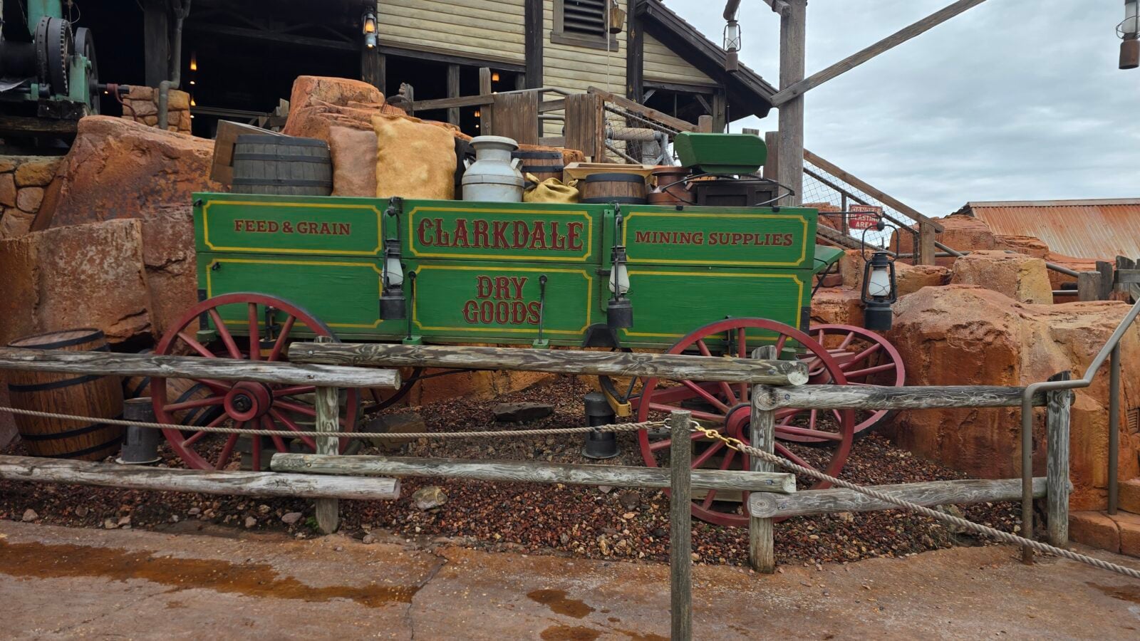 Green Clarkdale wagon labeled Dry Goods with Feed  Grain and Mining Supplies in a rustic mining display red wheels nearby