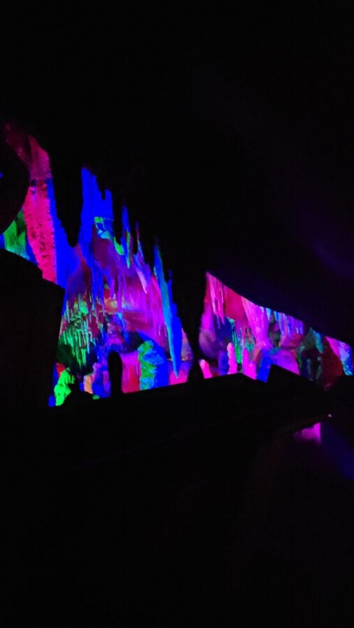 Inside a dark cave with colorful illuminated ice formations and icicles in pink blue and green hues