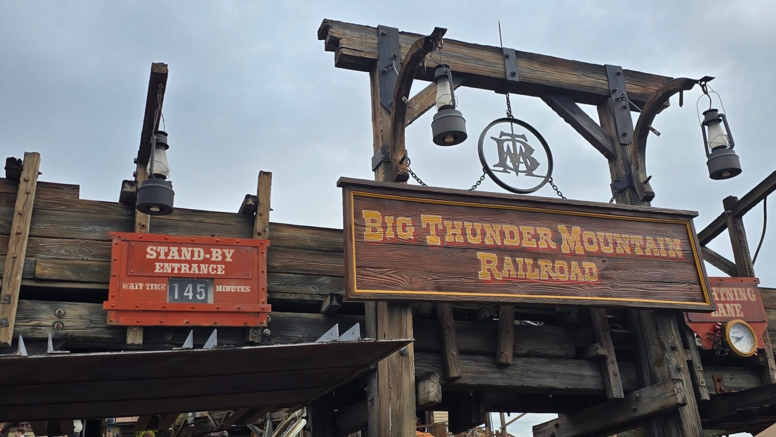 Wooden rails and signs for Big Thunder Mountain Railroad with lanterns and a rustic circular logo hanging above the entrance sign