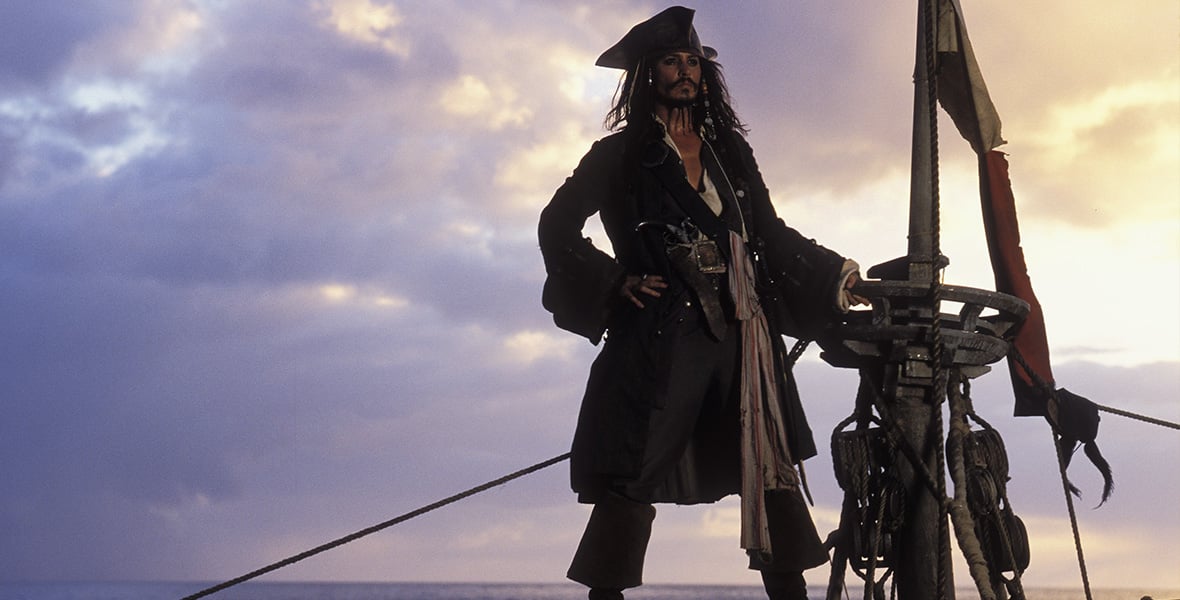 Pirate captain standing on a ships deck at sunset hands on hips wearing a tricorn hat and long coat