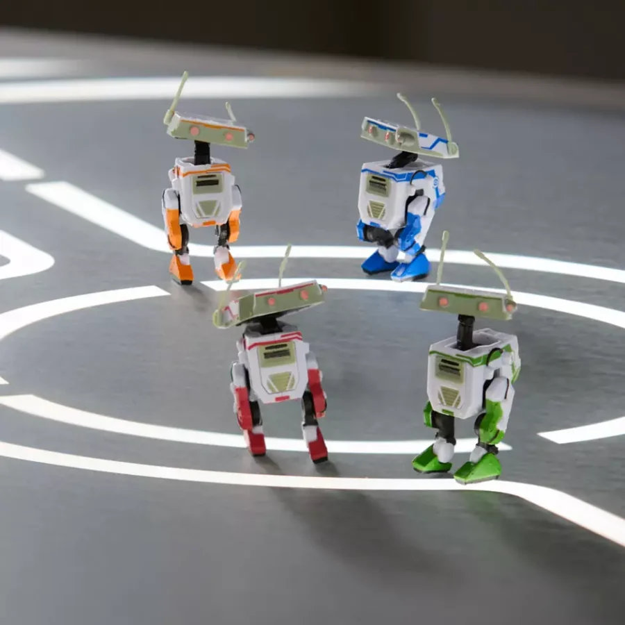 Four small toy robots with springy antennae standing on a gray track marked with white lines appearing to face off in a mini arena