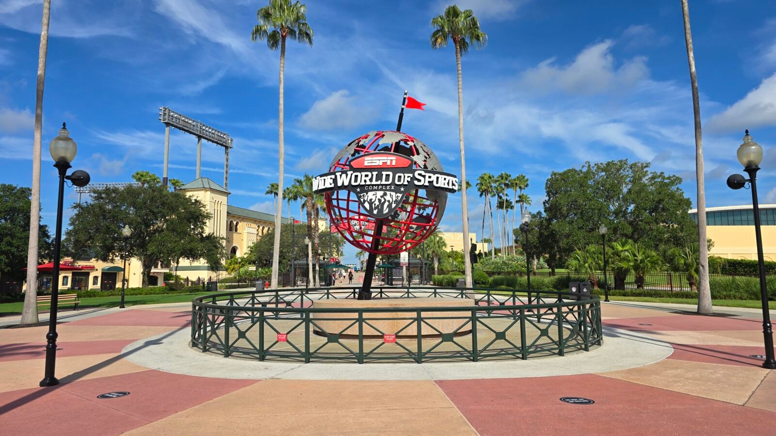 Spherical globe sculpture with ESPN Wide World of Sports sign at center palm trees and buildings in a sunny park setting
