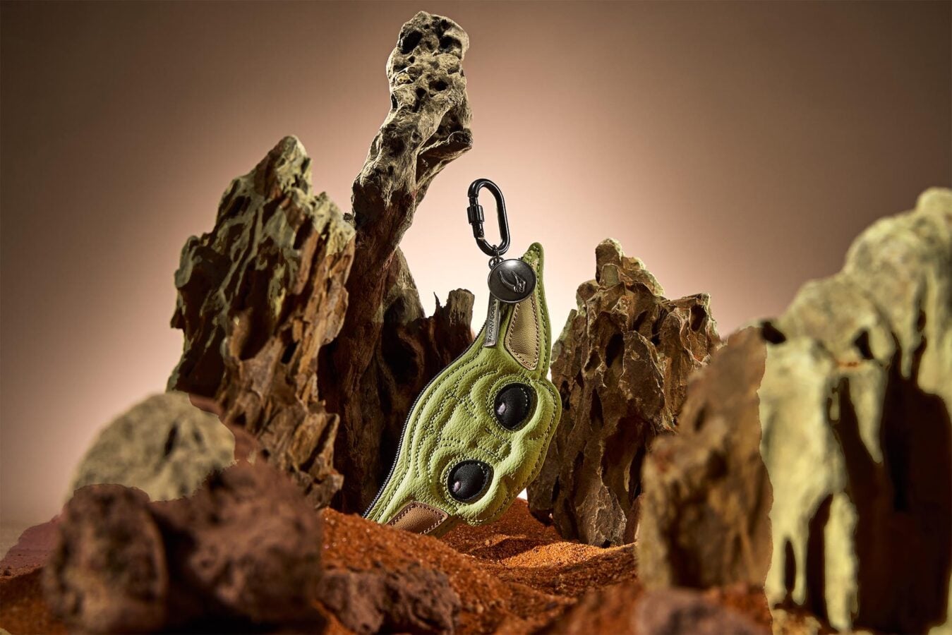 Green hiking shoe with a black carabiner attached resting among jagged rocks with a warm brown background