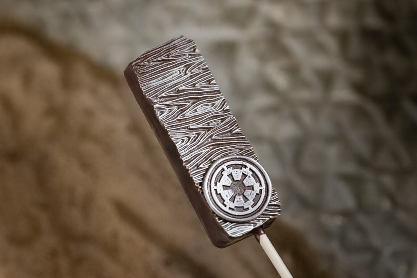 Close up of a chocolate bar on a stick with a wood grain pattern and an Imperial crest emblem on the front