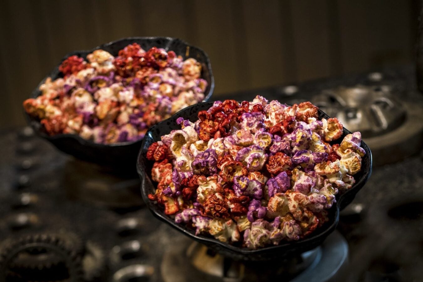 Two black bowls filled with colorful popcorn purple red white on a dark metal surface
