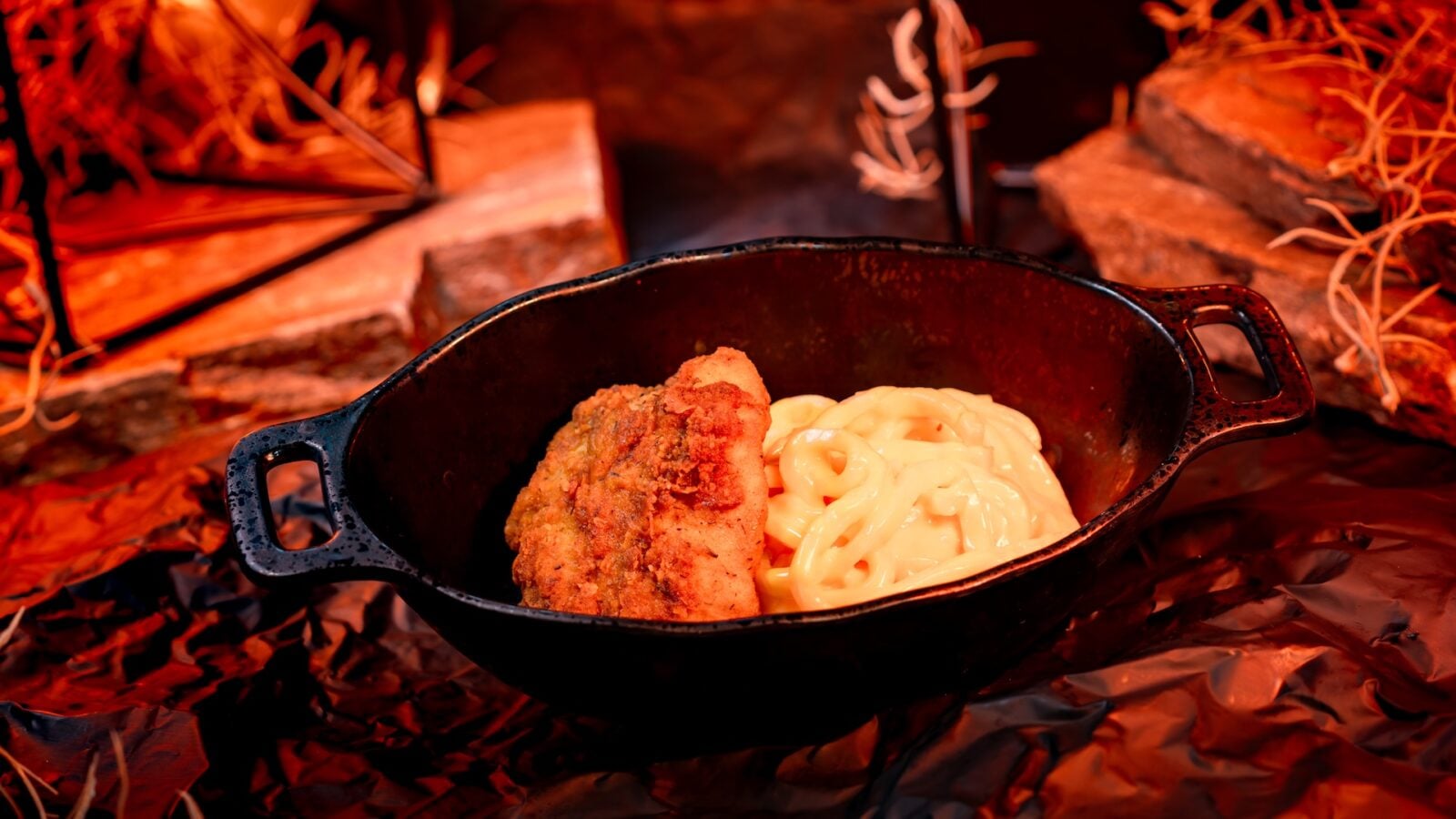 Cast iron skillet with fried chicken and creamy pasta over a warm campfire