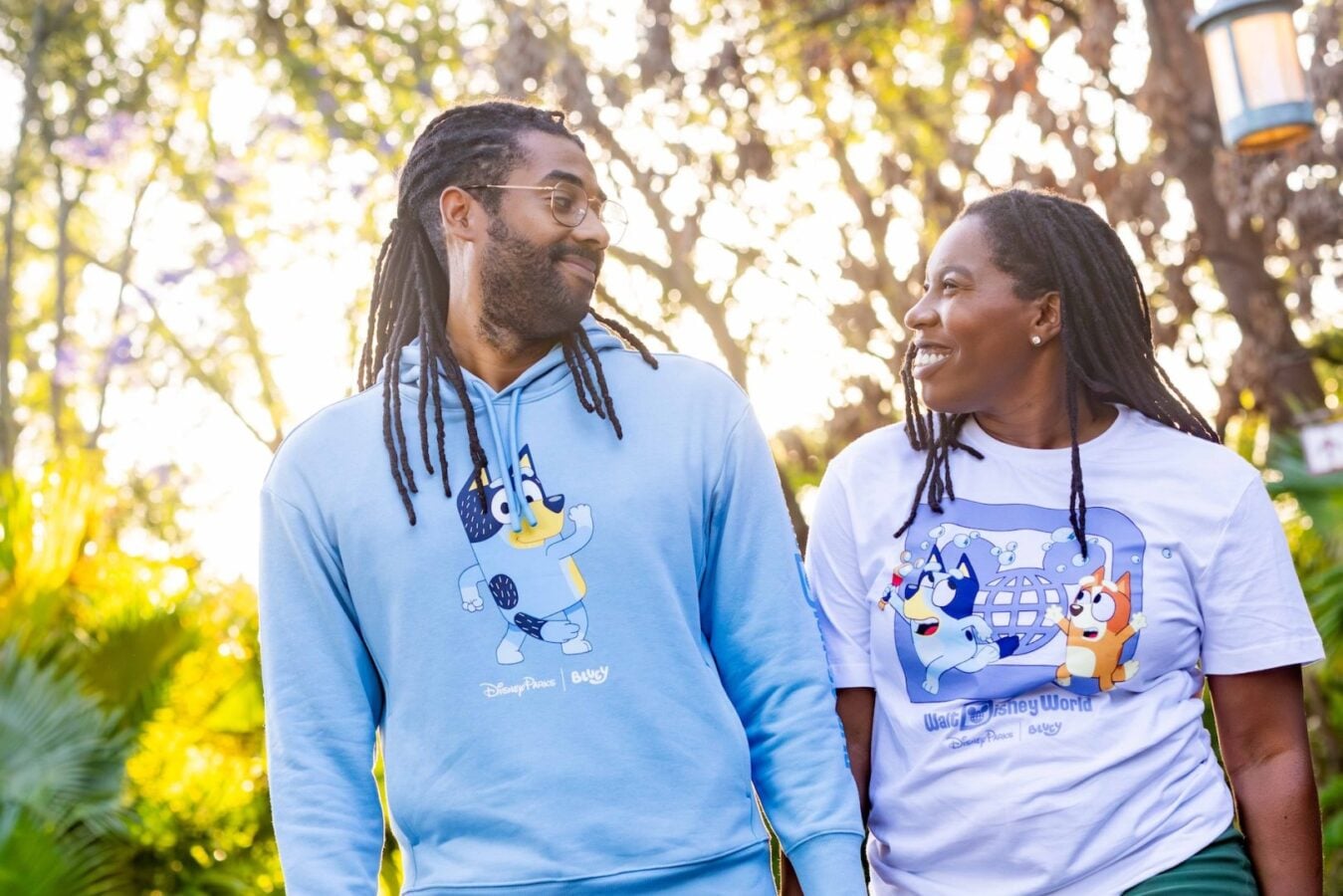 Two people walk outdoors on a sunny day smiling at each other wearing Disney themed sweatshirts