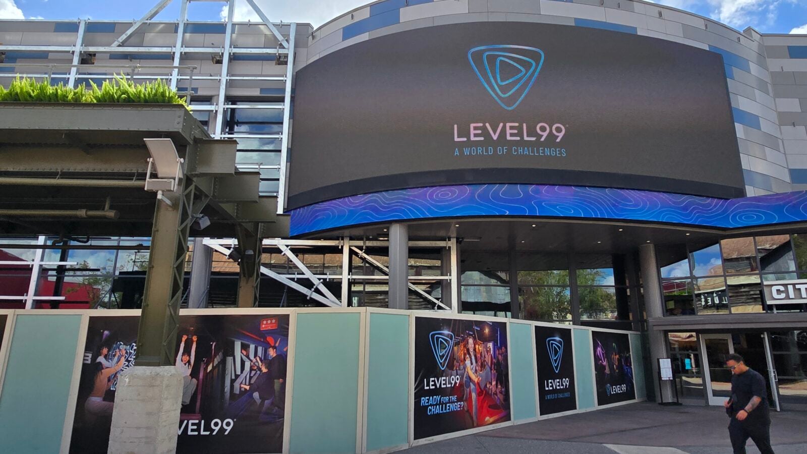 Front of LEVEL99 venue showing a curved digital sign with the LEVEL99 logo and A World of Challenges plus a blue decorative band and entrance posters
