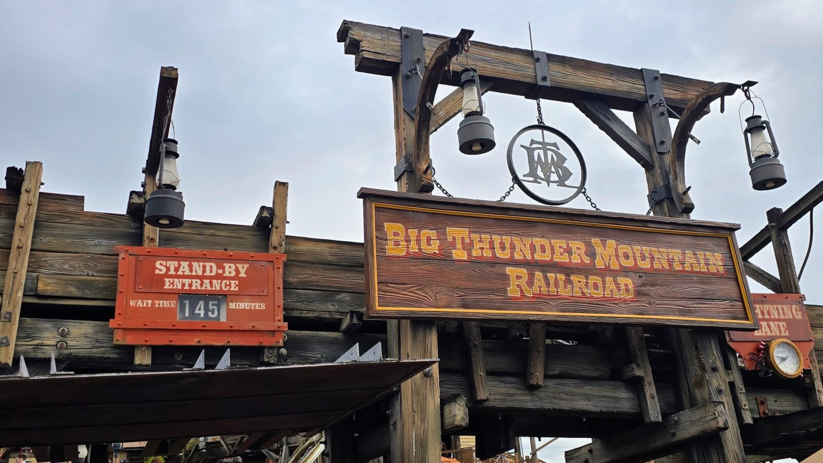 Rustic wooden entrance sign for Big Thunder Mountain Railroad with hanging lanterns and a Stand By Entrance sign showing a 145 minute wait time