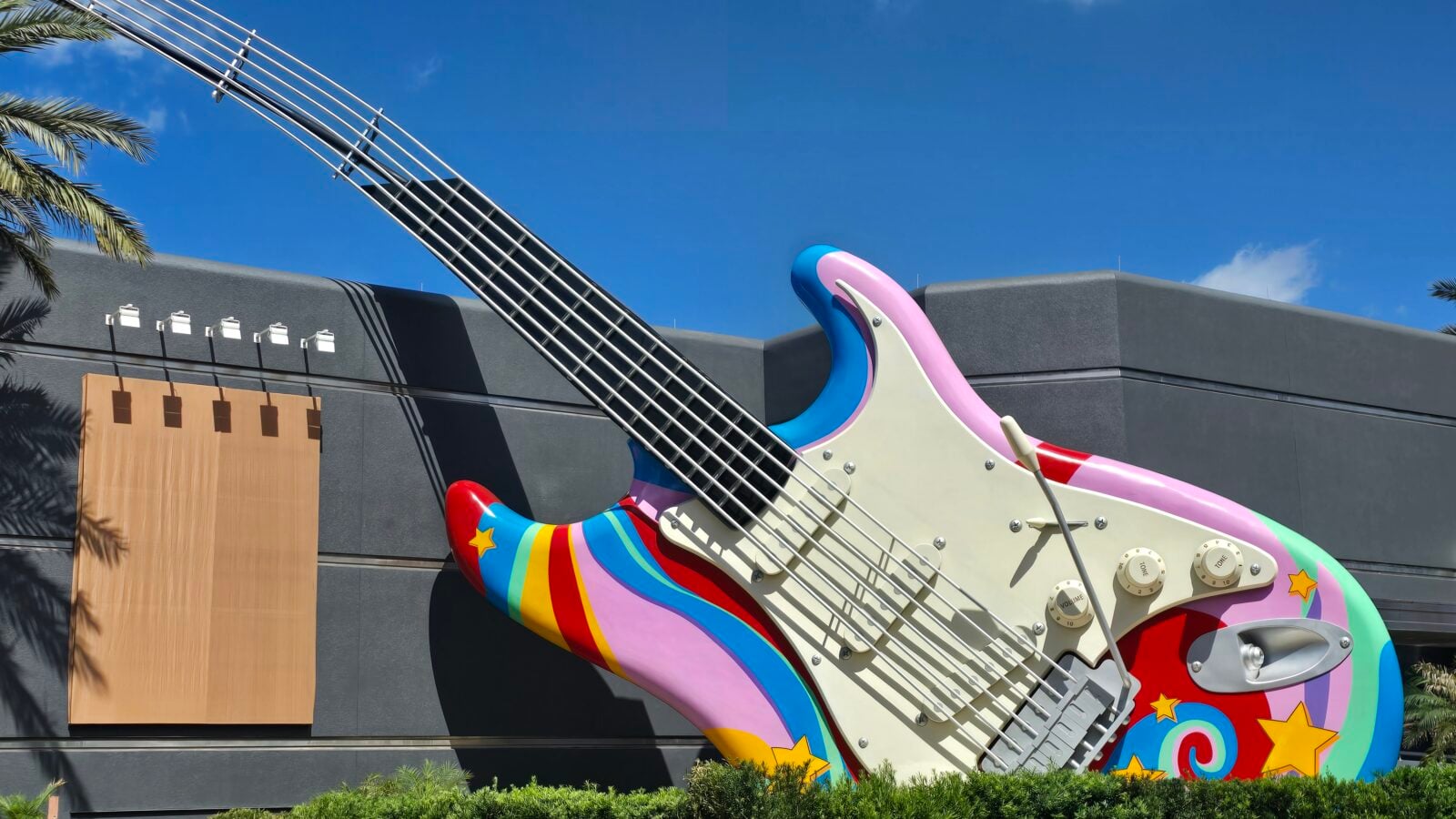 Oversized colorful guitar sculpture outdoors against a gray building and blue sky