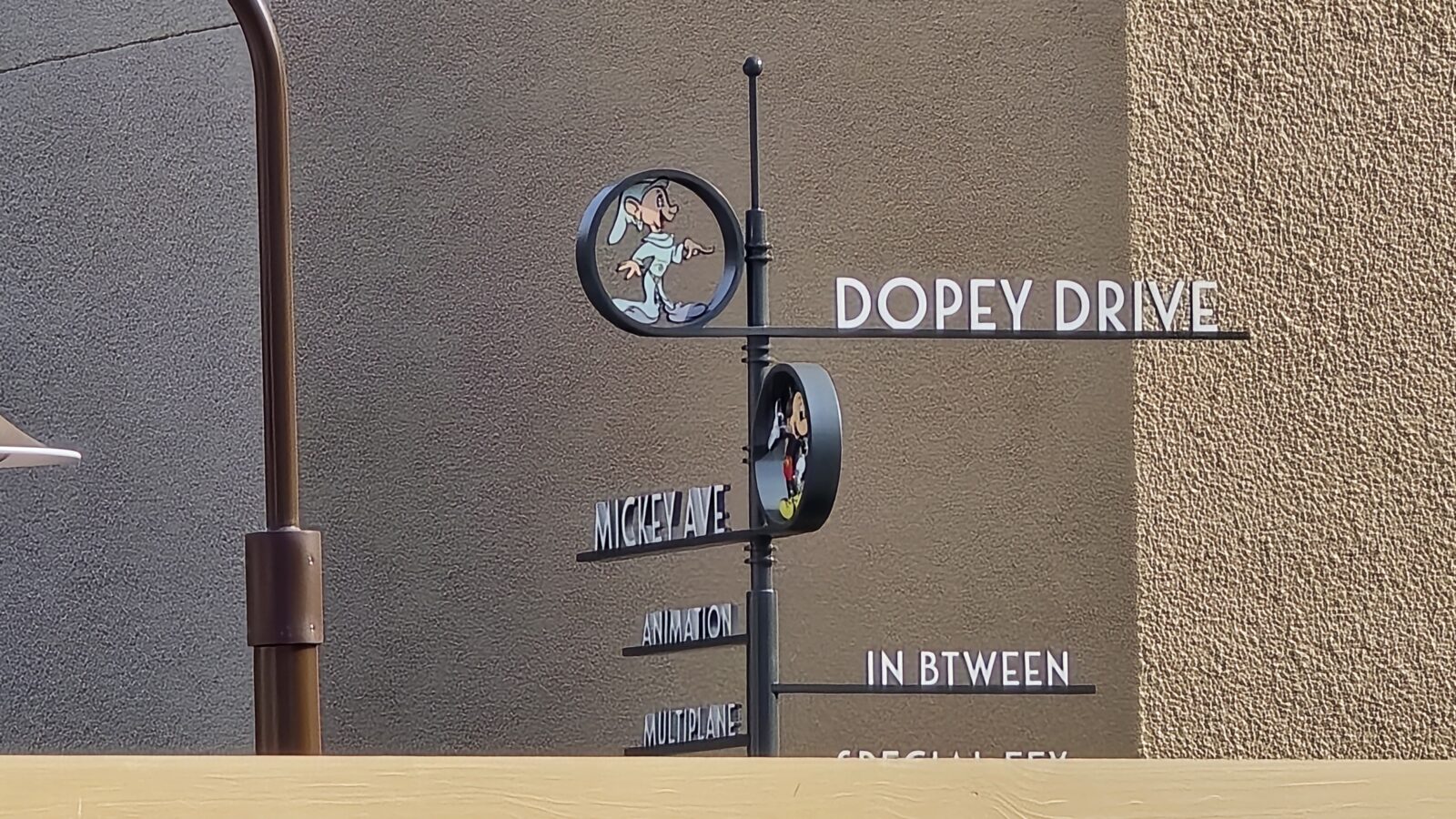 20260512090806 Fantasy Land News Street sign showing Dopey Drive and Mickey Ave with a circular Dopey illustration badge nearby