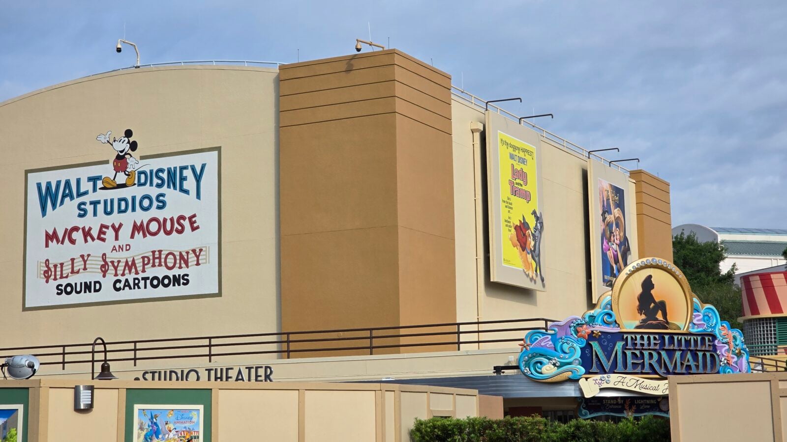 20260512090930 Fantasy Land News Facade of a Disney themed entertainment complex with large posters WALT DISNEY STUDIOS MICKEY MOUSE AND SILLY SYMPHONY SOUND CARTOONS featuring Mickey Mouse and colorful posters for Lady and the Tramp and The Little Mermaid on the walls