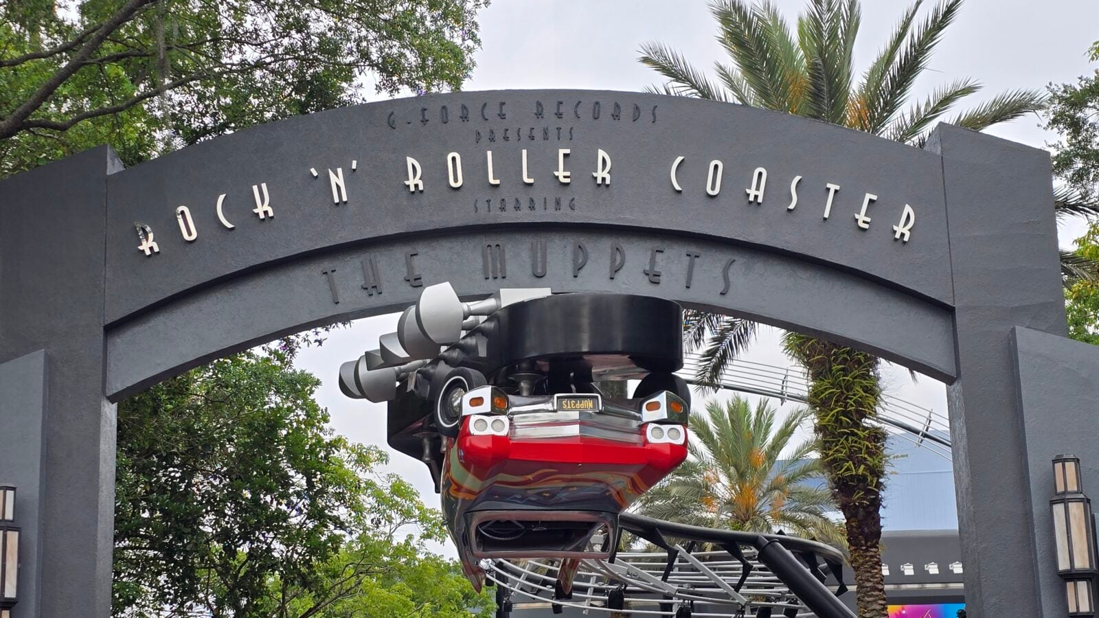 20260512093117 Fantasy Land News Arched sign for Rock N Roller Coaster with a red roller coaster train passing overhead against palm trees and greenery