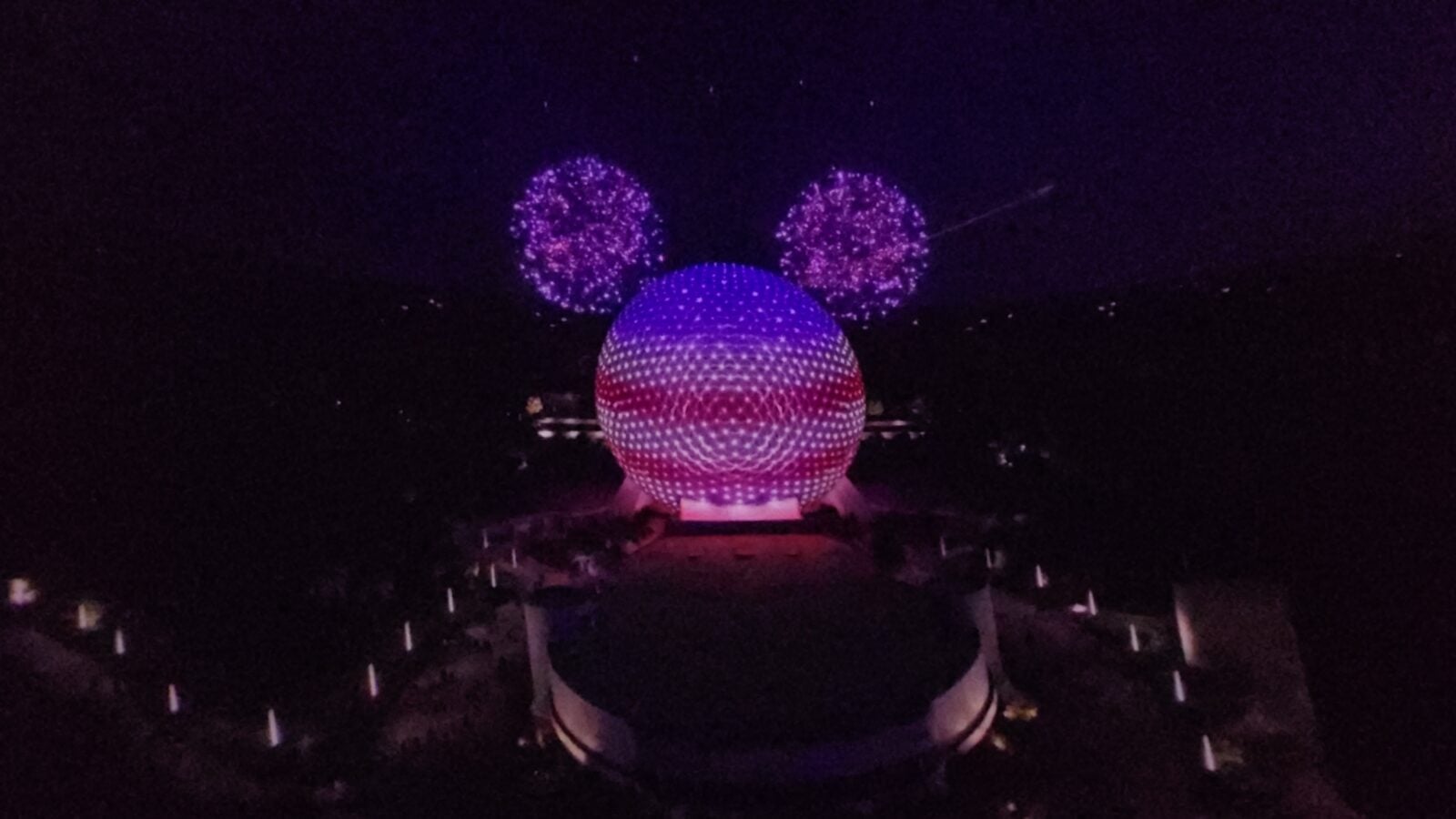 202605161027220 Fantasy Land News Person wearing glowing purple Mickeystyle ears at night with a large illuminated purple sphere and its reflection in water in the foreground