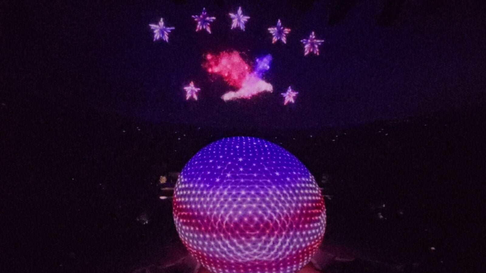 20260516102725 Fantasy Land News Person wearing a glowing purple geodesic LED hat at night with fireworks in the dark sky behind