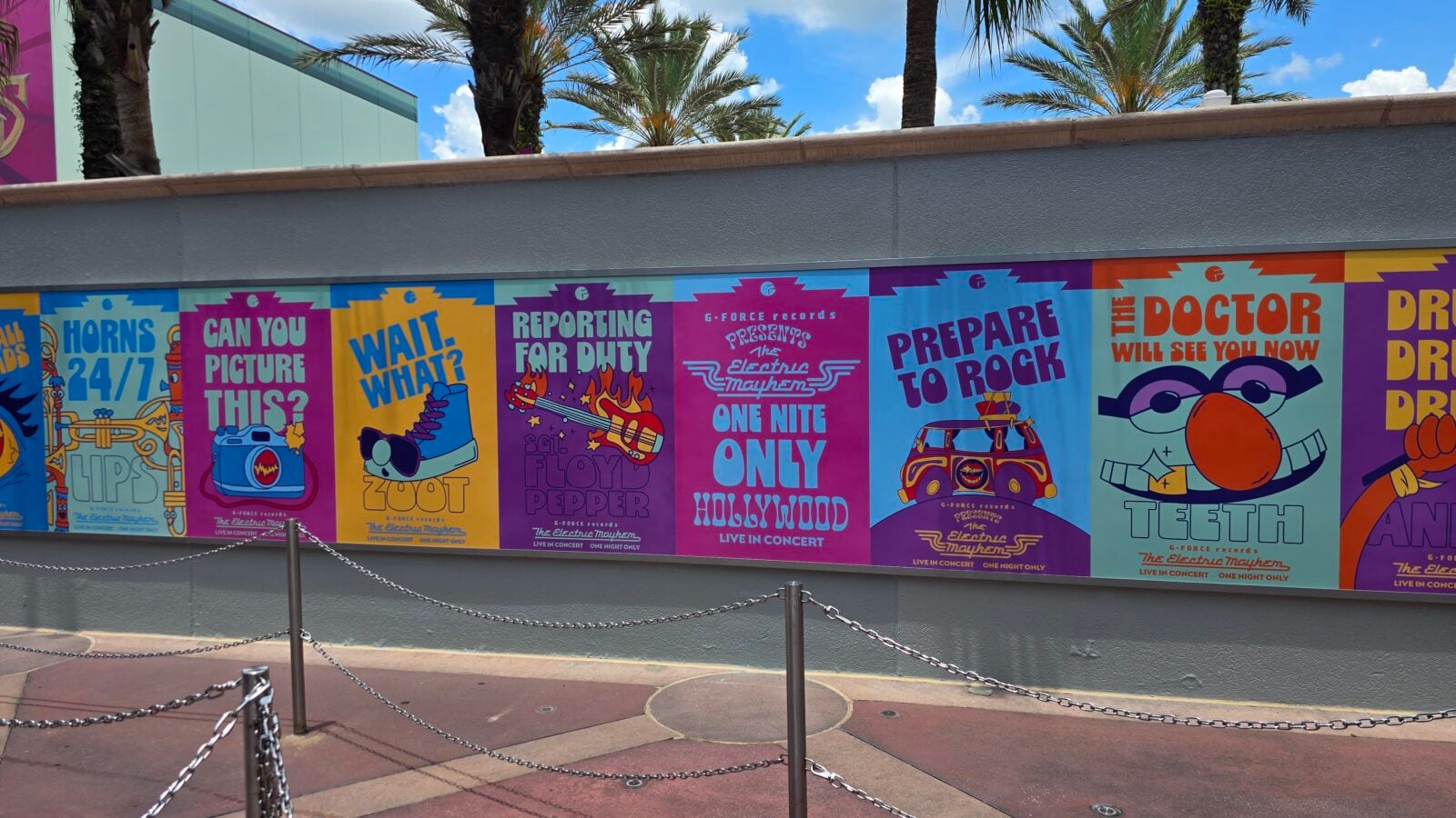 Colorful row of posters advertising music events on a wall with palm trees and a blue sky in the background