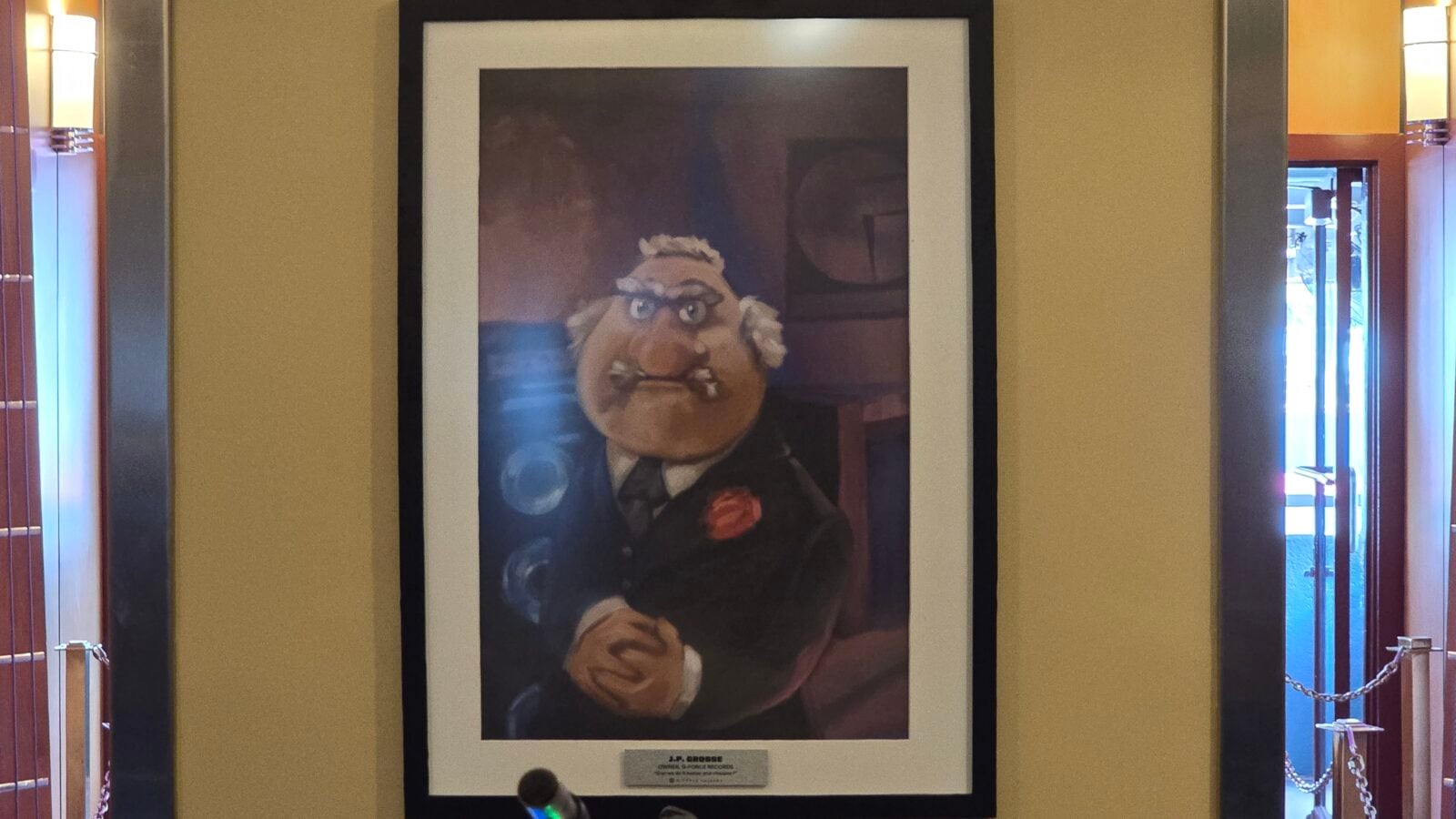 Framed portrait of an elderly man with glasses in a tuxedo displayed in a museum case