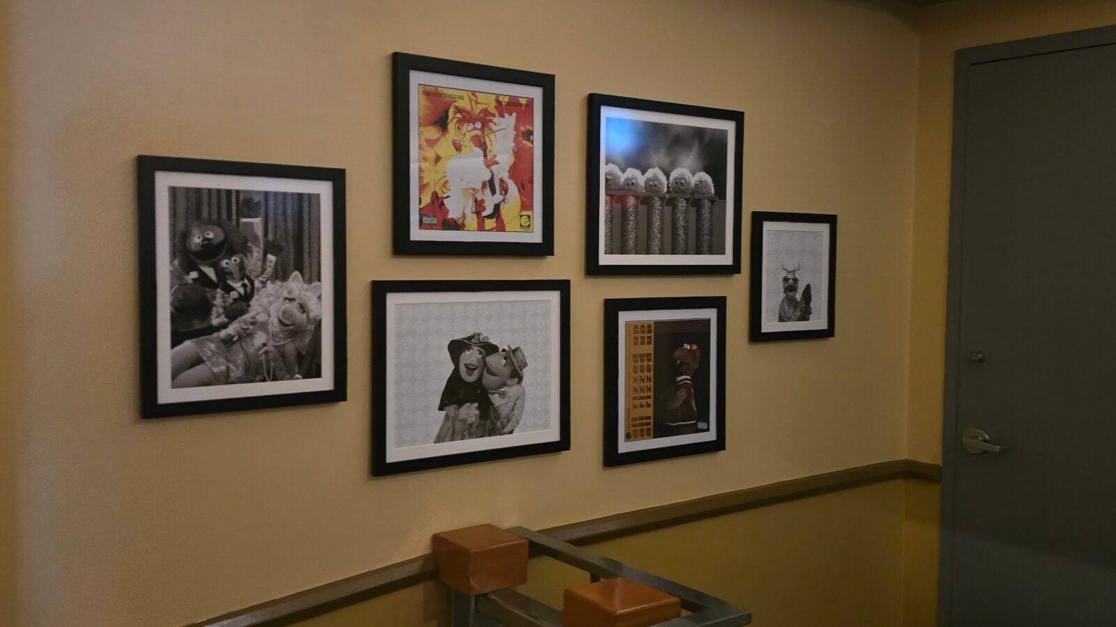 Hallway wall displaying six framed prints of cartoon puppets arranged in a grid on a beige wall