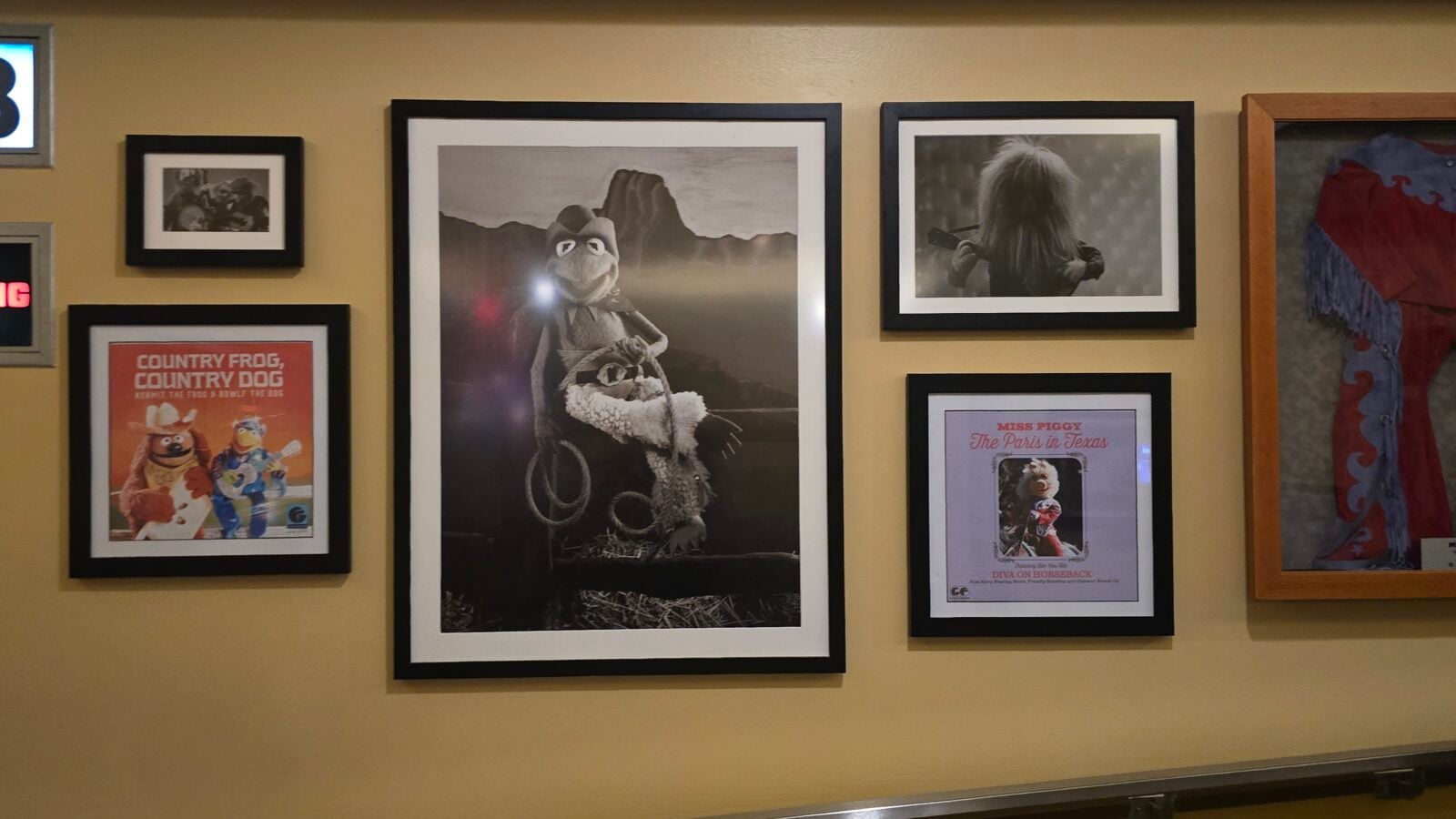 Wall gallery with multiple framed prints on a yellow wall a large black and white Muppet photo dominates the center Descriptive poster to its left reads Country Frog Country Dogs