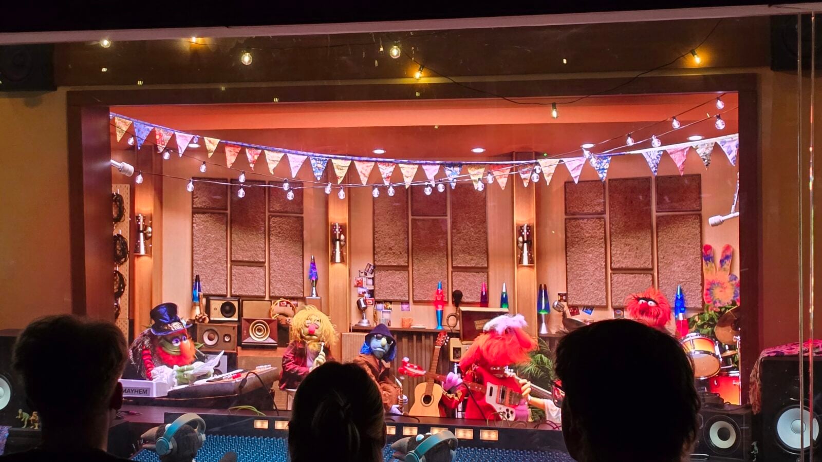 A colorful puppet show stage with string lights and triangular bunting guitars and speakers on the stage and puppet characters visible in the foreground