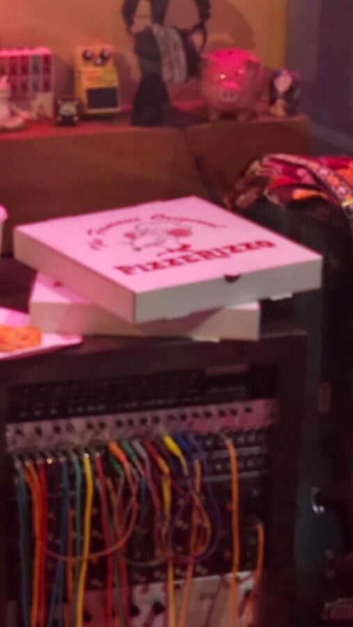Network equipment rack with many colorful cables and a pink tinted room a pizza box sits on top of the rack