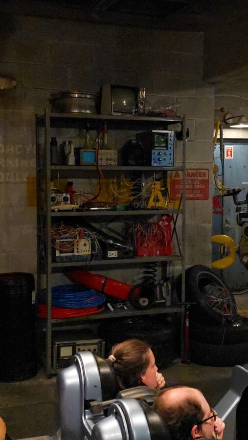 Industrial workshop with electronics on metal shelves cables and test equipment dim lighting and safety sign visible in the background