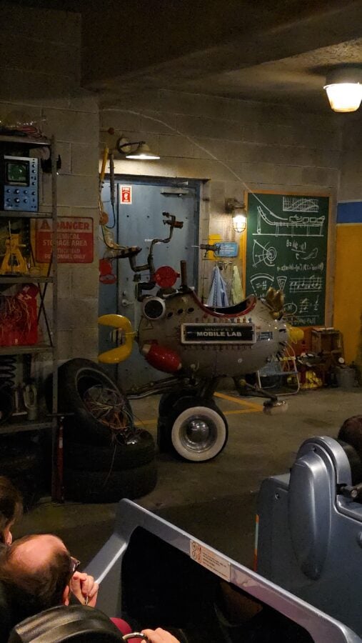 Industrial workshop scene with a gray rounded Mobile Lab vehicle chalkboard diagrams and assorted tools nearby
