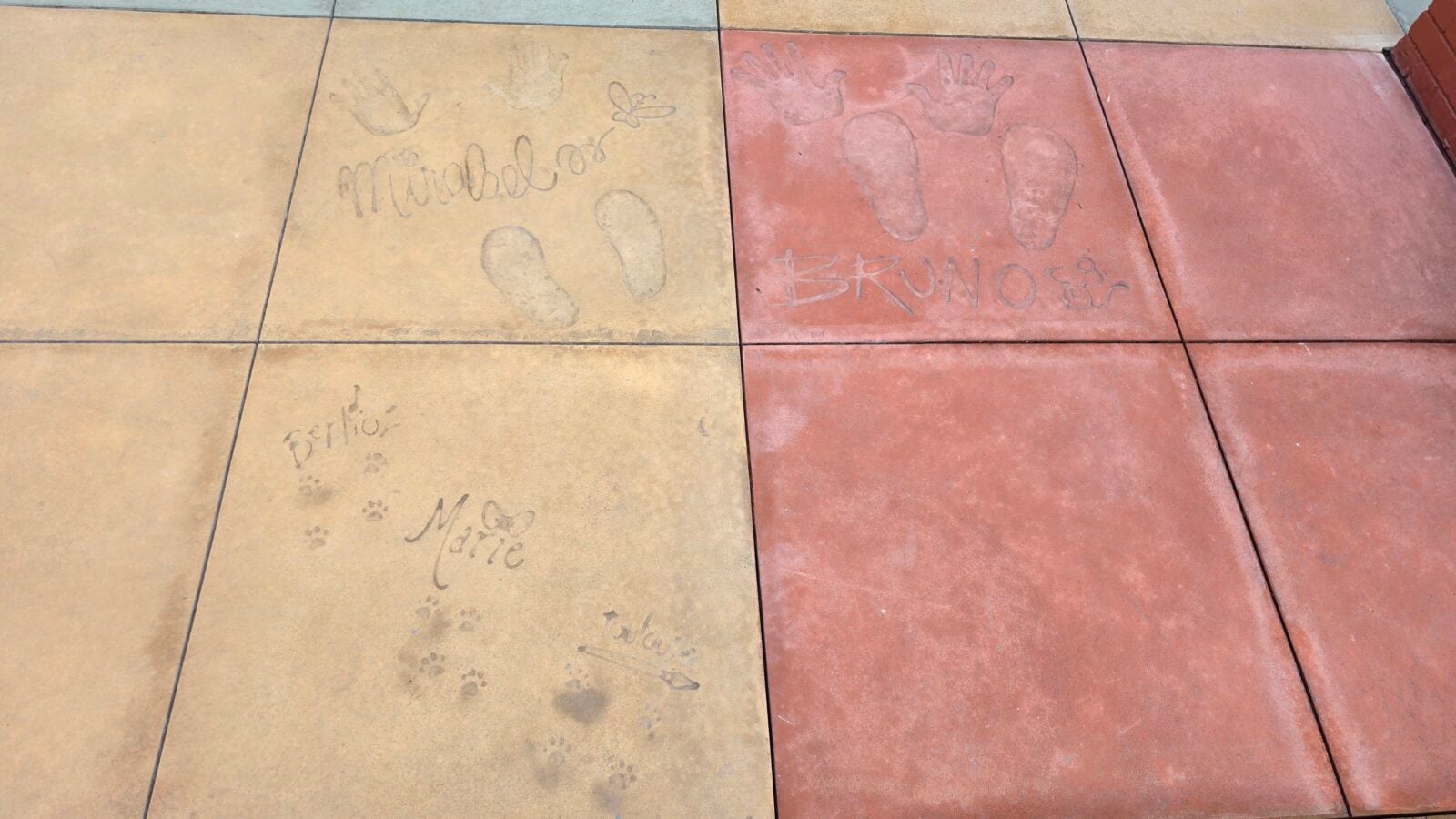 Tile walkway with imprinted footprints and handprints names like Michaela and Bruno are etched on the colored paving stones