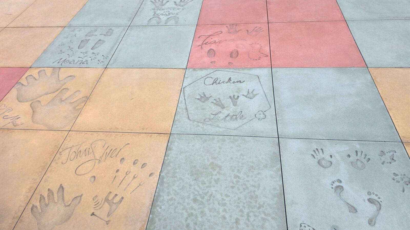 Colorful tiled sidewalk with handprints and footprints stamped in blue orange and gray tiles visible names like Moana and Chicken Little on the stones
