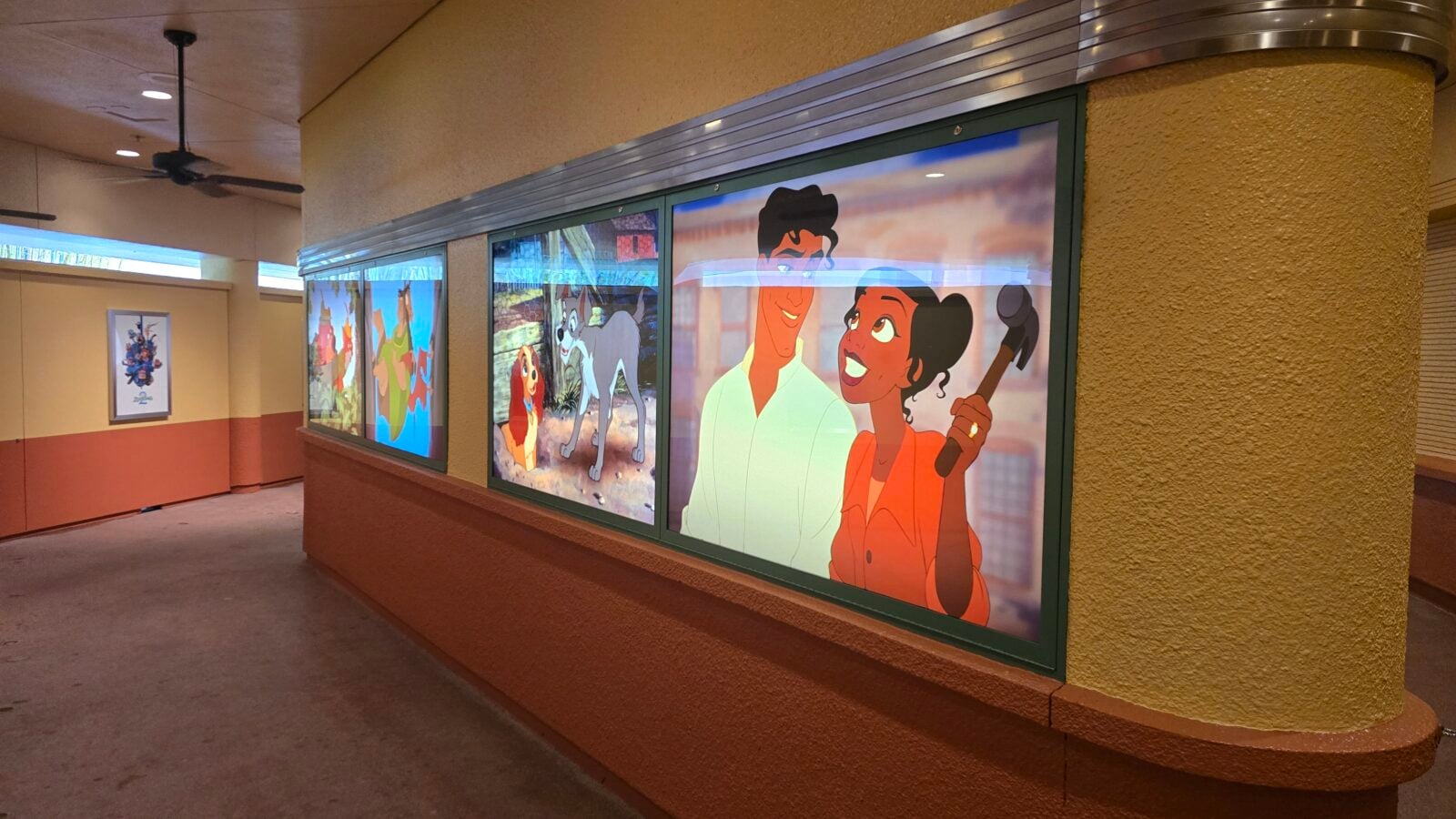 Indoor hallway with a row of large colorful cartoon posters displayed in glass panels along a tan textured wall