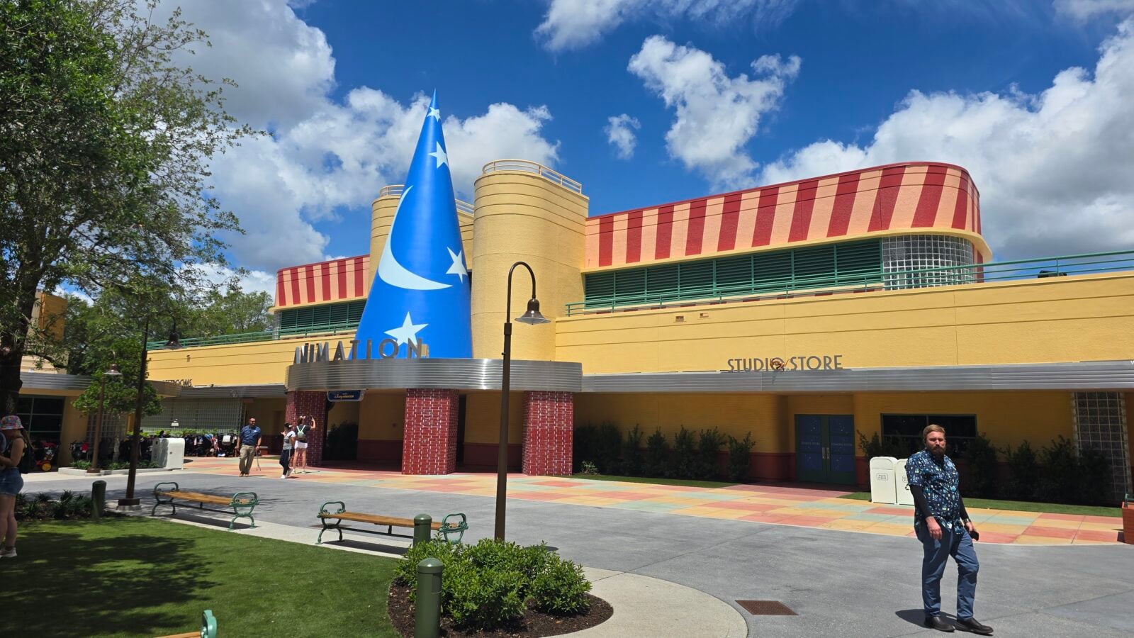Colorful retro style building with a tall blue cone sculpture featuring white stars yellow walls and people walking outside on a sunny day