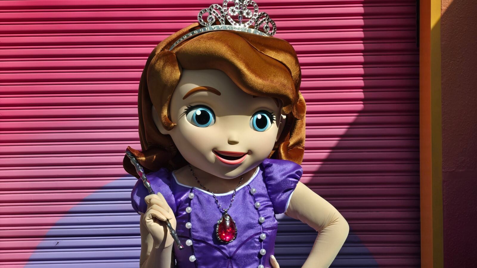 20260522100326 Fantasy Land News Cartoon princess statue with brown hair and a silver tiara wearing a purple dress in front of a pink roller shutter