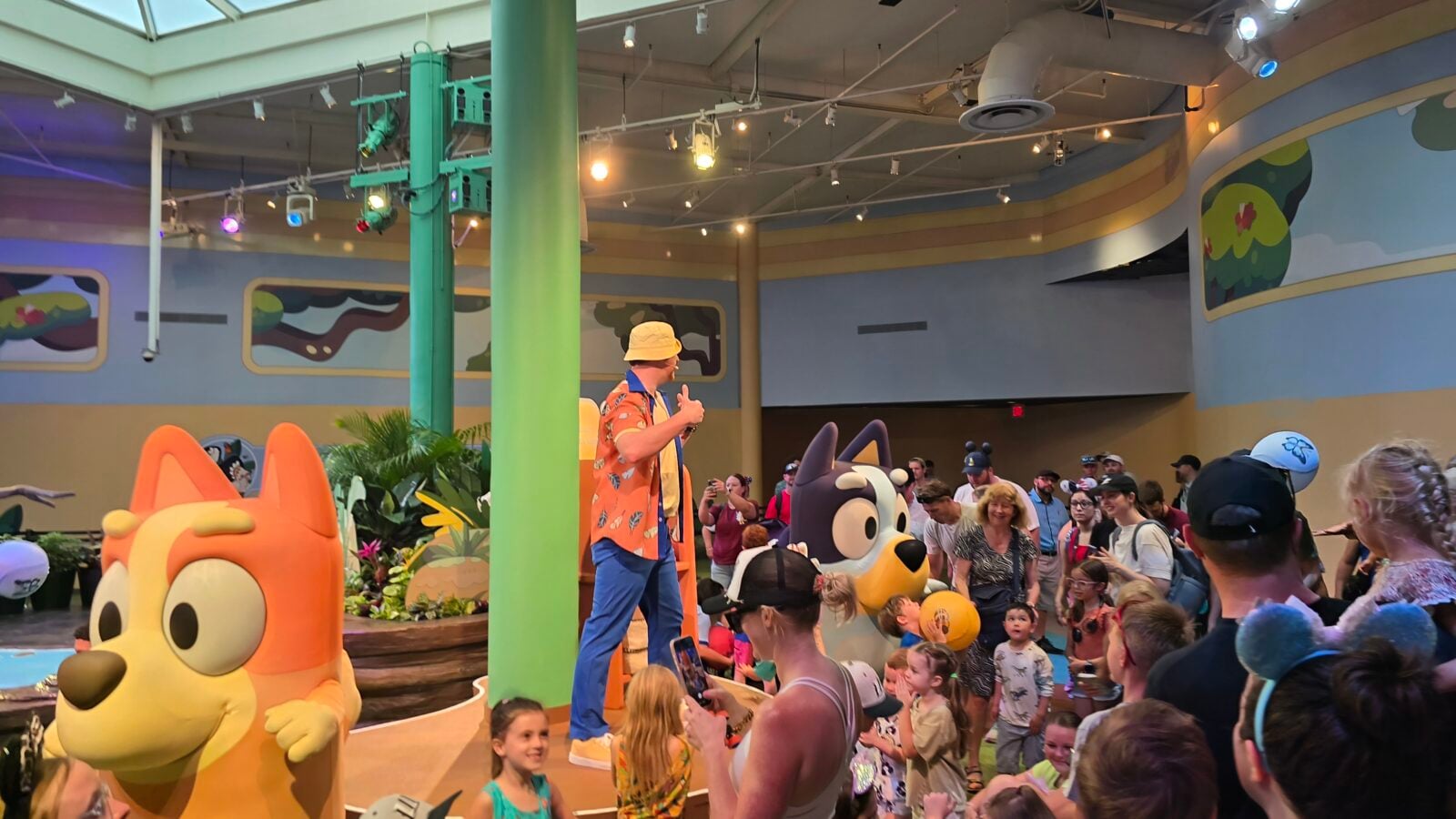 20260525110627 Fantasy Land News Crowd of children and adults watching a performer in a colorful indoor theme space with large cartoon animal mascots in the foreground