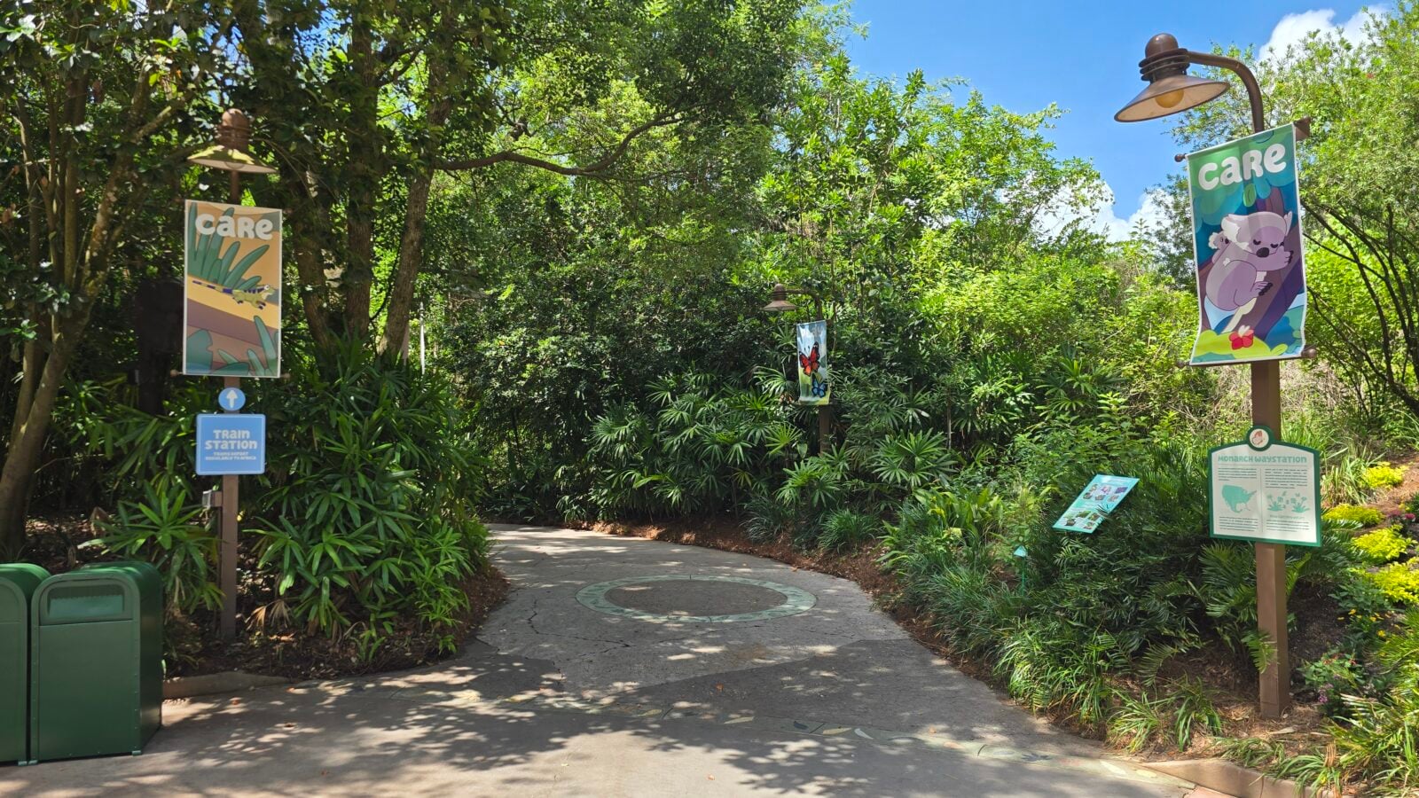 20260525112553 Fantasy Land News Lush walkway in a park with colorful animal banners on posts and a clear blue sky above