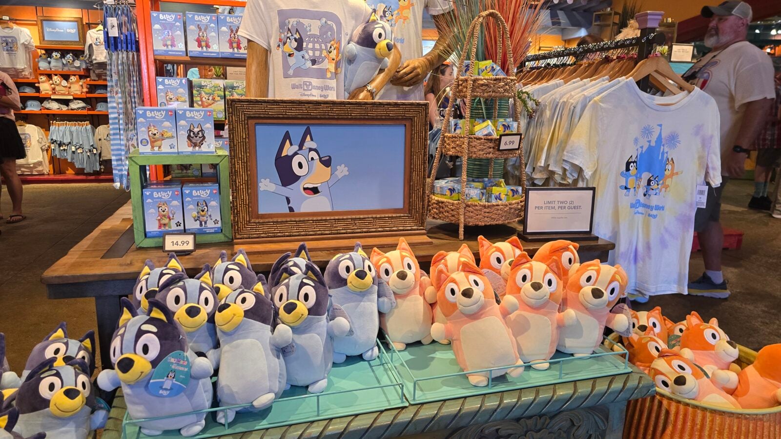 20260525123742 Fantasy Land News Colorful shop display of plush dog characters in blue and orange arranged on a table with shirts and merchandise in the background