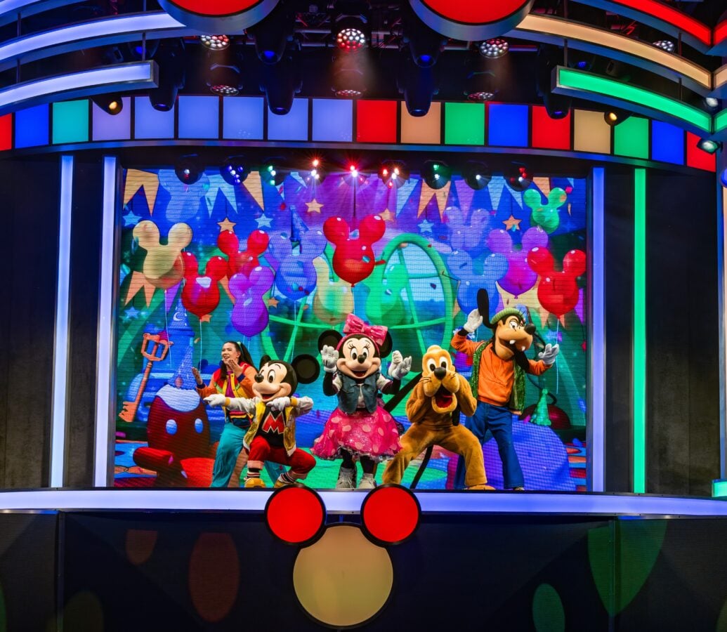 Colorful stage performance with Mickey Mouse Minnie Mouse and friends dancing amid a bright balloon filled backdrop