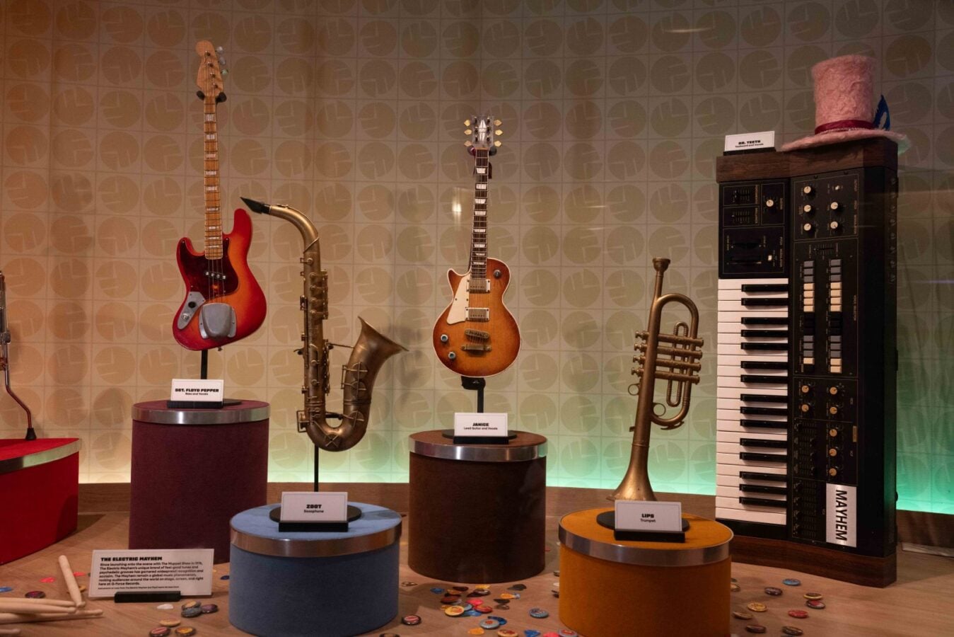Museum display of vintage instruments red electric guitar saxophone sunburst guitar trumpet and a large keyboard on the right top hat sits atop the cabinet